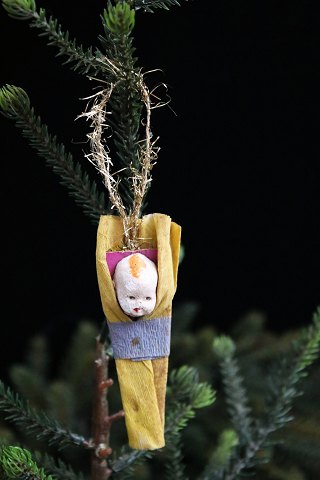 Gammelt juletræspynt fra omkring år 1940 i form af lille barn svøbt i klæde 
lavet i pap , gips og papir.