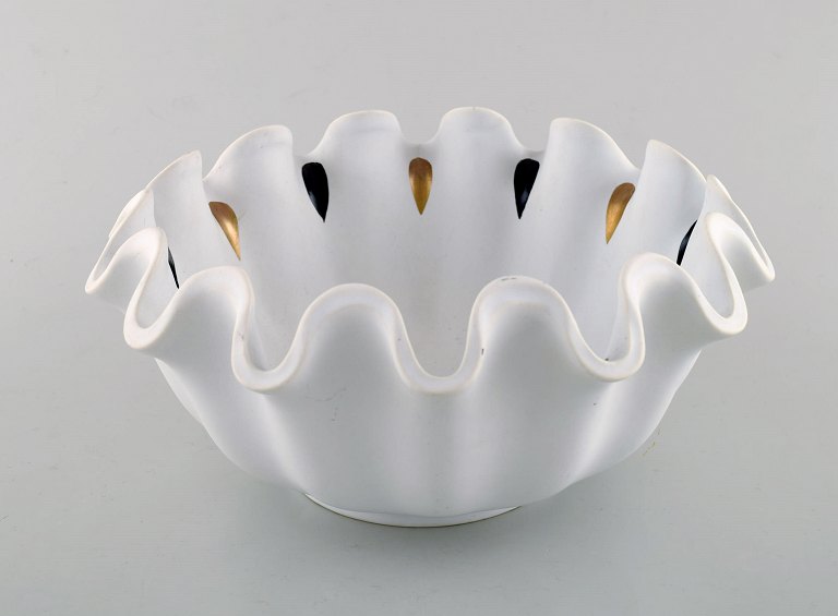 Wilhelm Kåge for Gustavsberg. Large curved bowl in glazed ceramic with ruffled edge. Hand painted black and gold. Mid 20th century.