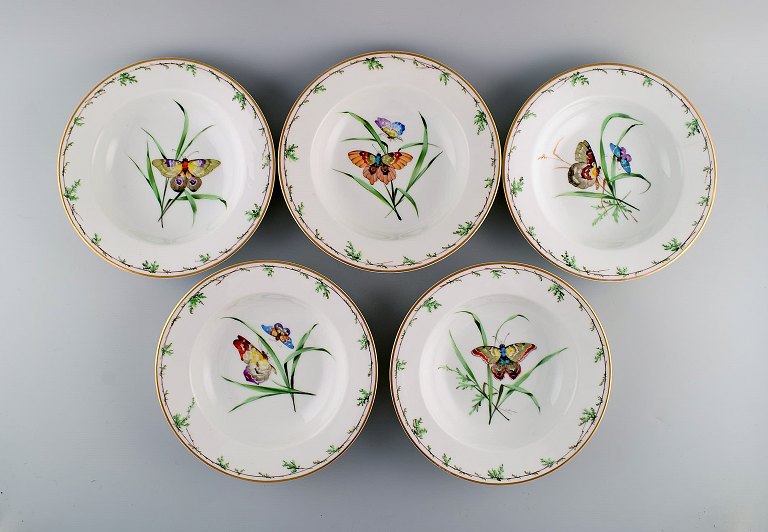 Five antique Royal Copenhagen deep plates in porcelain with hand-painted flowers, butterflies and gold edge. Mid-19th century.